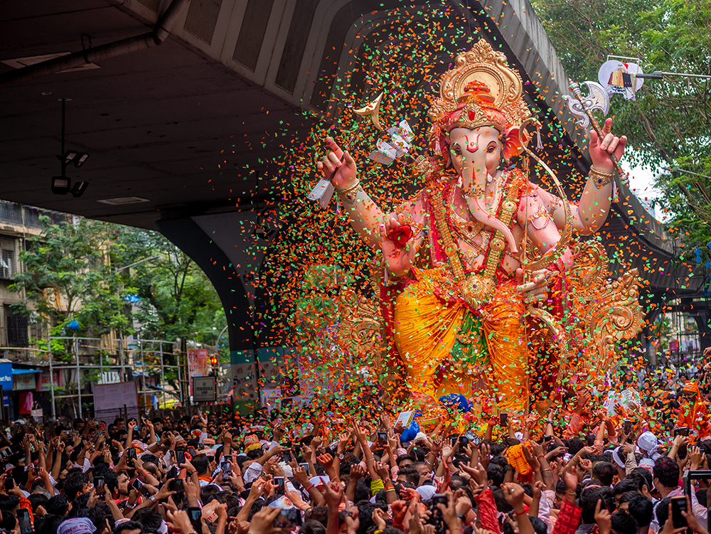 A grand multicultural public parade with a two-story Ganesh covered in confetti in a Ganesh Chaturthi festival celebration.